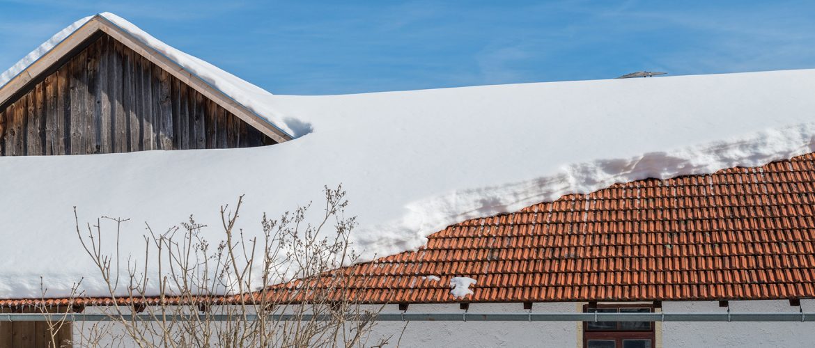 Dach eines großen Scheunen- und Wohngebäudes mit viel Schnee, von dem eine Dachlawine abgegangen ist.