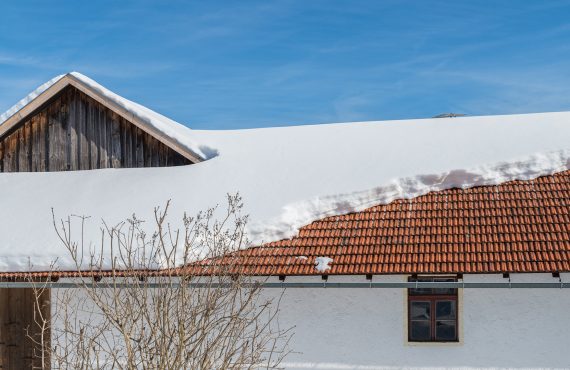 Dach eines großen Scheunen- und Wohngebäudes mit viel Schnee, von dem eine Dachlawine abgegangen ist.
