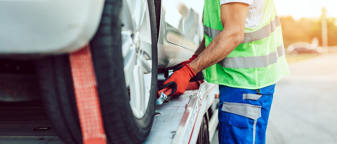 Eine Person mit Warnweste sichert ein Auto auf einem Abschleppwagen.
