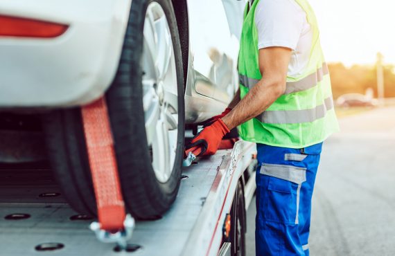 Eine Person mit Warnweste sichert ein Auto auf einem Abschleppwagen.