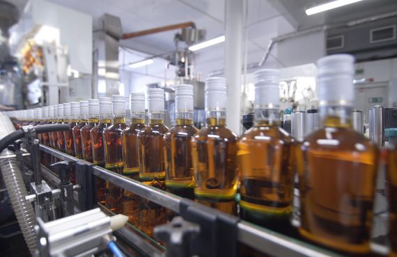 Auf einer industriellen Abfüllanlage stehen Flaschen in einer Reihe. Der Inhalt ist eine leicht braune Flüssigkeit.