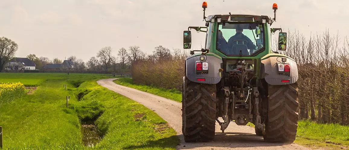 Rückansicht eines Traktors, der auf einem Feldweg fährt.