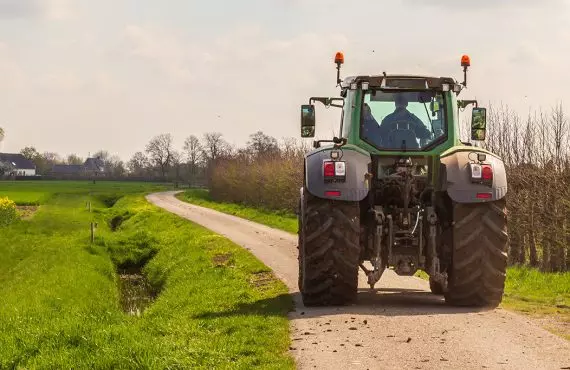 Rückansicht eines Traktors, der auf einem Feldweg fährt.