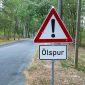 Landstraße im Wald. Ein Verkehrsschild steht am rechten Rand und weißt auf eine Ölspur hin.