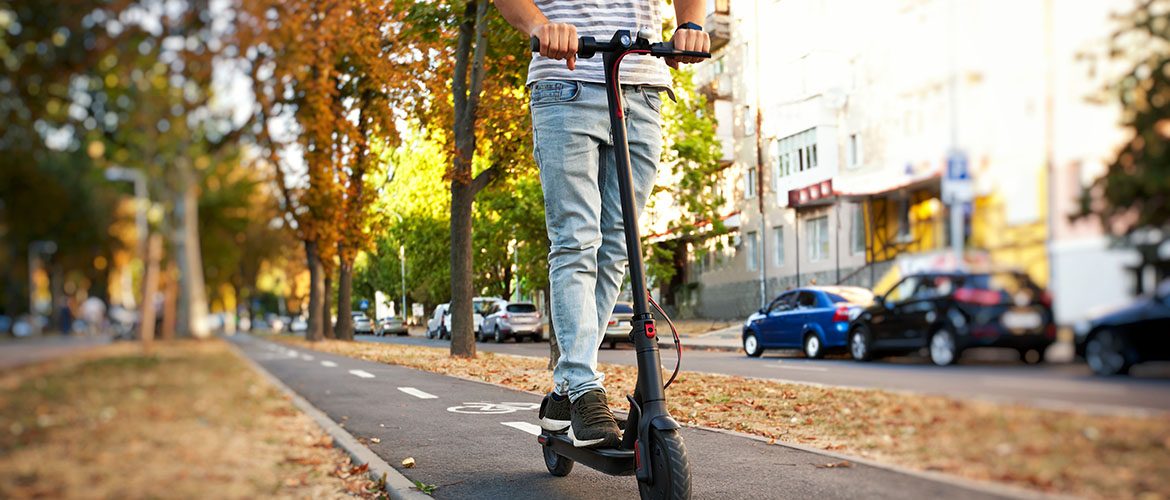 Ein junger Mann fährt mit dem Elektroroller durch die herbstliche Stadt.