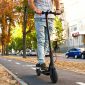 Ein junger Mann fährt mit dem Elektroroller durch die herbstliche Stadt.